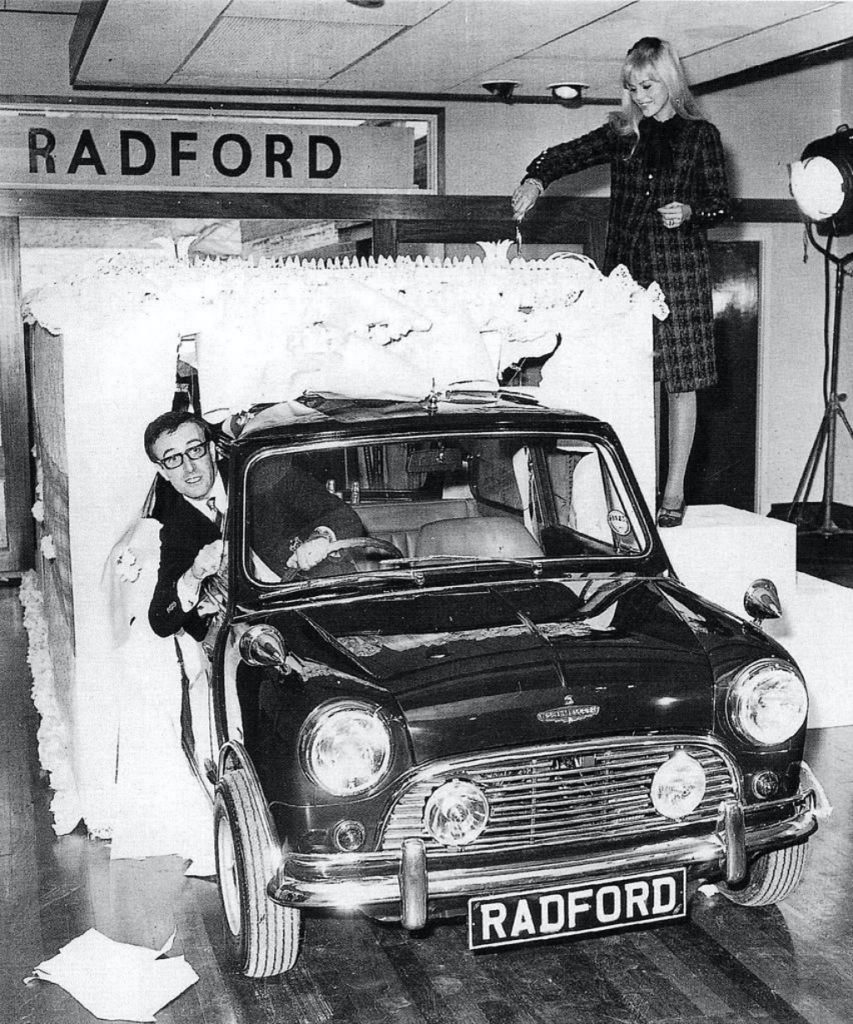 Peter Sellers con su nuevo Mini mientras su mujer Brit Ekland corta la tarta de celebración del 2º aniversario de la tienda de Radford Coach el 7.10.1965 | Wesley/Keystone