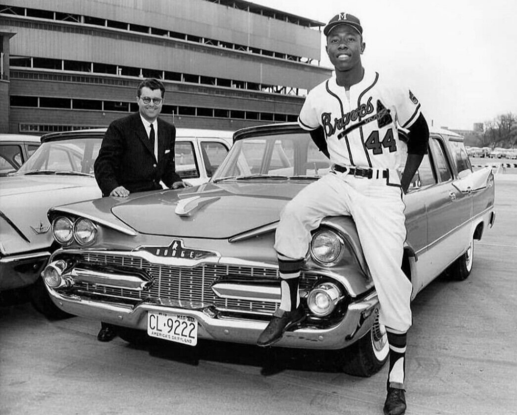 El jugador de baseball Hank Aaron posa junto a un Dodge Station Wagon de 1959