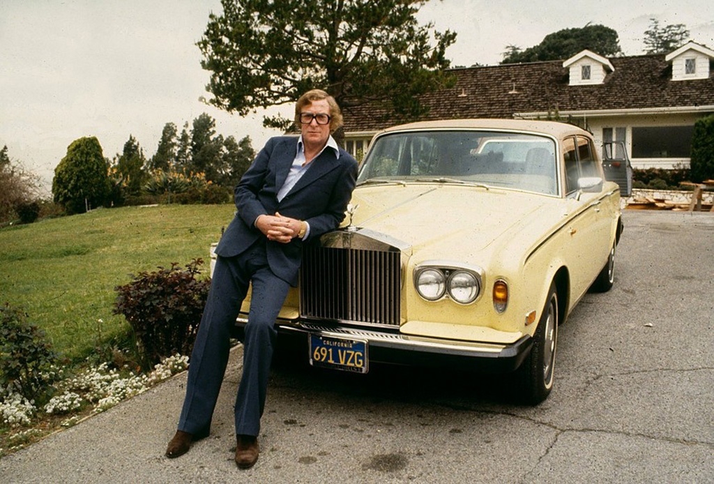 Personajes singulares y sus coches: Michael Caine apoyado en su Rools Royce Silver Shadow II en su casa de Beverly Hills en 1982 | Getty Images